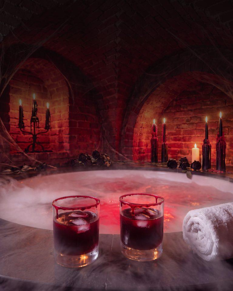 Vířivka v cihlových katakombách s mlhou, černými svícemi a dvěma tmavě červenými nealko drinky